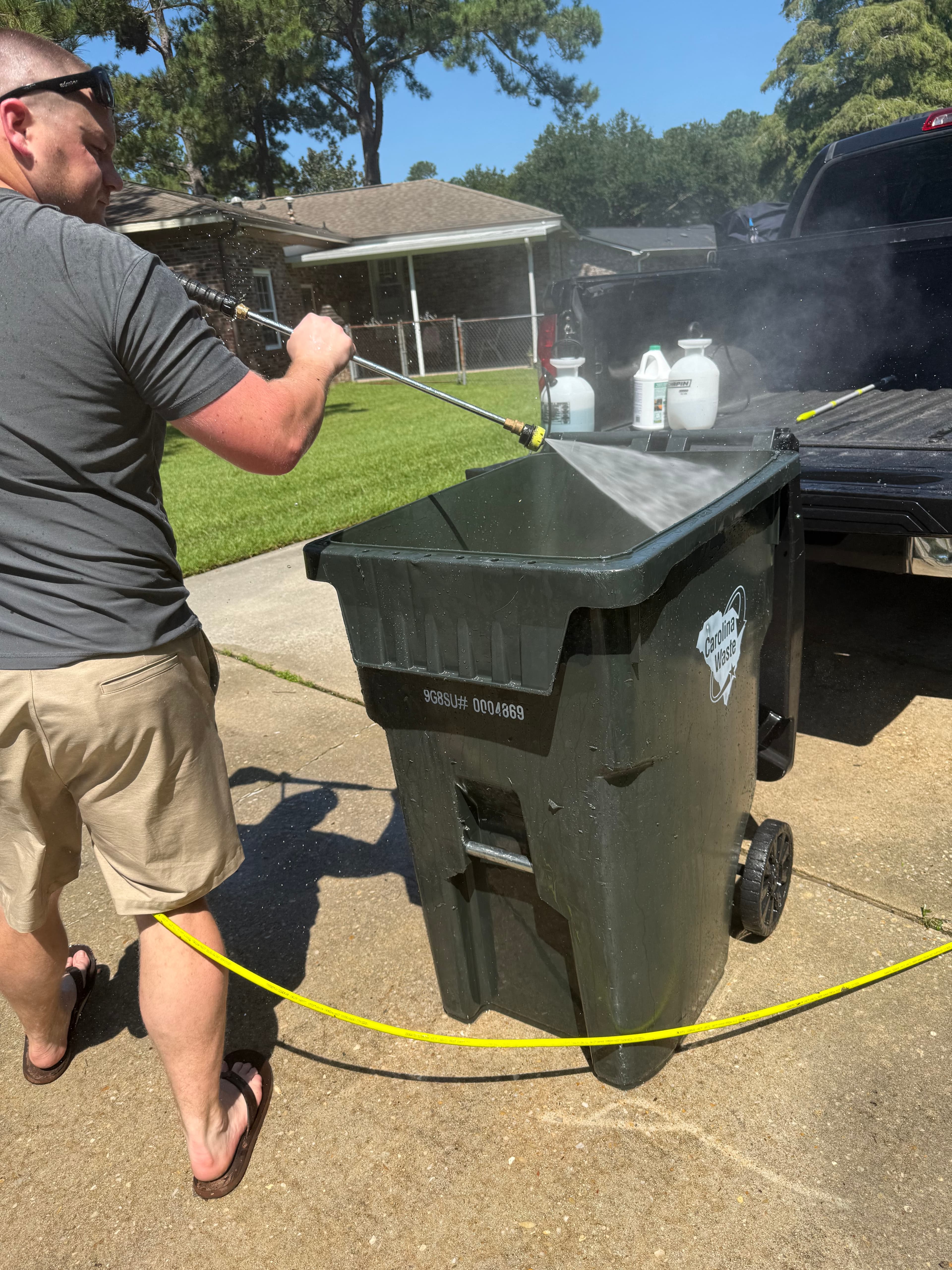 Clean Curb Co. pressure washing a residential garbage bin on a driveway.